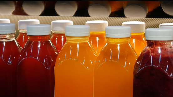 Many beautiful plastic bottles of various natural juices in a store shelf close-up