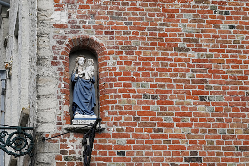 Bruges, Belgium - September 13, 2022: The facade of a historic building with an architectural detail depicting human figures in the form of a small statue