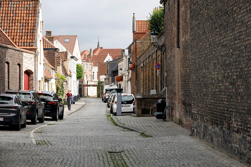 Bruges, Belgium - September 13, 2022: A narrow cobbled street between rows of brick houses. Cars are parked here and someone is walking somewhere in the distance