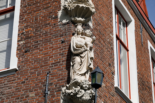 Bruges, Belgium - September 12, 2022: The facade of a historic building with an architectural detail depicting human figures in the form of a small statue
