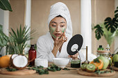 Attractive asian woman looking at mirror sitting at table with ingredients for homemade cosmetics