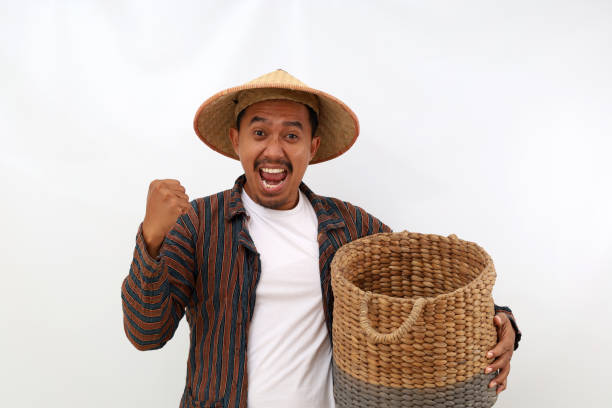 Happy asian farmer standing while holding an empty basket and clenching his hand. Isolated on white background