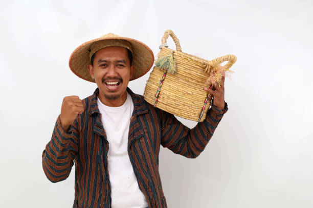 istock Happy asian farmer standing while holding an empty basket on his shoulder and clenching his hand. Isolated on white background 1444794656