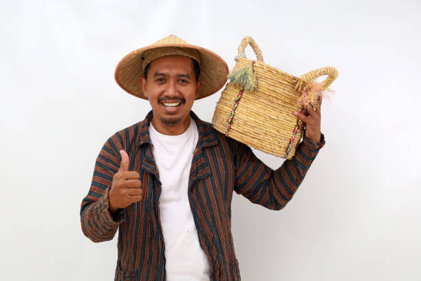 istock Happy asian farmer standing while holding an empty basket on his shoulder and showing thumbs up. Isolated on white background 1444794657