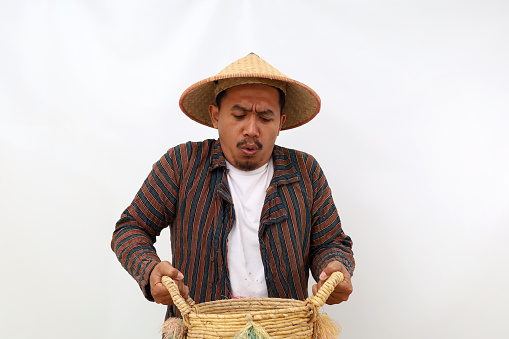Asian farmer standing while holding a heavy basket. Isolated on white background