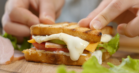 Making a sandwich with ham, salad, ripe tomato slices and pieces of cheese. Fast food concept.