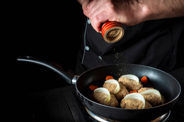 istock Cooking cutlets on grill pan by chef hands on black background for copy space text restaurant menu. The chef adds pepper 1444796139