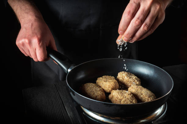istock Cooking cutlets on grill pan by chef hands on black background for copy space text restaurant menu. The chef adds salt 1444796243