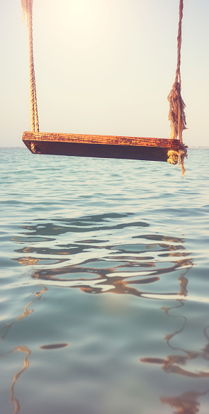 An old wooden swing above the water, selective focus, color toning applied.