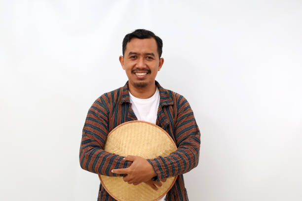 Happy asian farmer standing while carrying a hat and looking at the camera. Isolated on white background