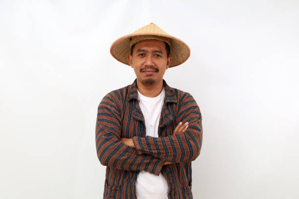 Happy asian farmer standing with a hat and folded hands while looking at the camera. Isolated on white background