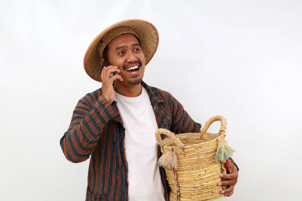 istock Happy asian farmer standing while talking on the phone and holding a basket. Isolated on white background 1444800438