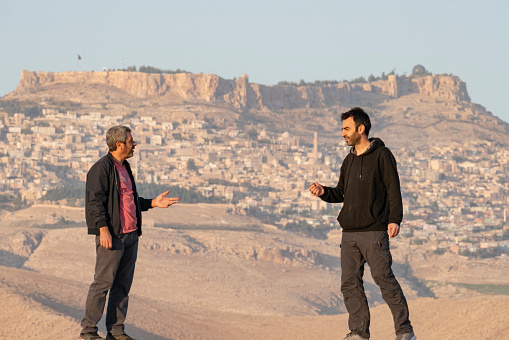 Brothers chatting in front of the view of Mardin.  Historical Mardin city center located on the top of the mountain. Shot with a full-frame camera on a sunny day.