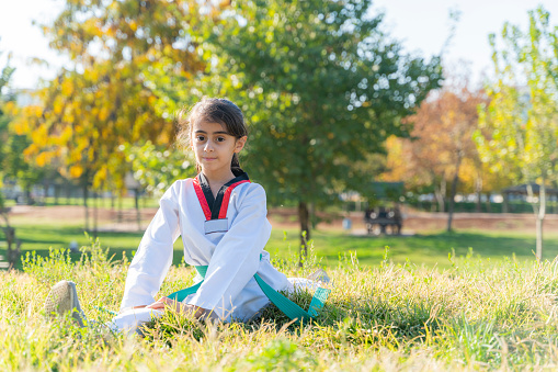 girl doing taekwondo training on grass in public park. long haired girl in taekwondo outfit is doing sports. in the woods and on the grass. Shot with a full-frame camera on a sunny day.