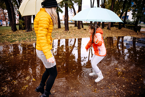 Mother and daughter jump on leaves and puddles
