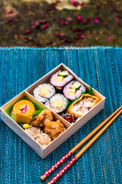 A cherry blossom themed bento box placed under cherry tree with a place mat, during flower season of cherry tree at a farm in Taichung, Taiwan.
