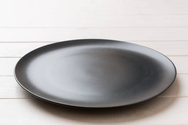 istock Perspective view of empty black plate on wooden background. Empty space for your design 1444823451