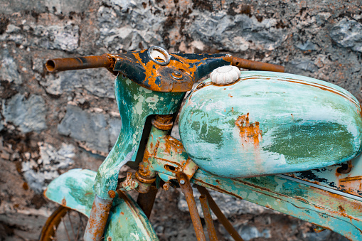 an old rusty motorcycle of turquoise color stands disassembled against the background of a stone staircase. Close-up of the rusty details of an old two-wheeler.