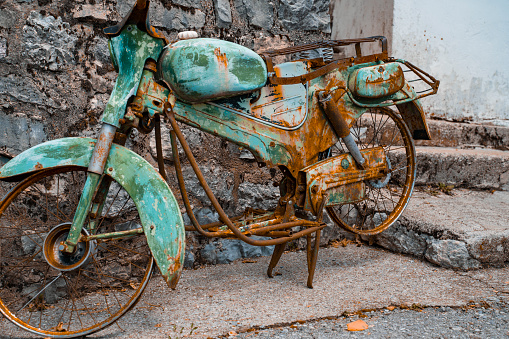 an old rusty motorcycle of turquoise color stands disassembled against the background of a stone staircase. Close-up of the rusty details of an old two-wheeler.