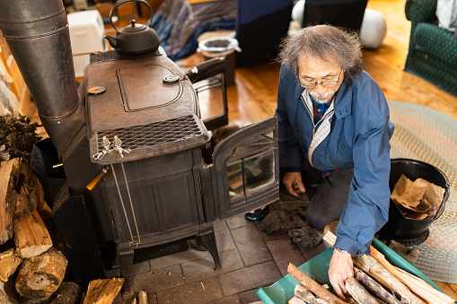 A senior Japanese man loads up his rustic fireplace in his log cabin house as the winter temperatures start dropping.