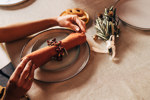 A from above view of an unrecognizable Caucasian female putting a napkin on a plate and decorating the table for holiday lunch. (cropped photo, rustic style)