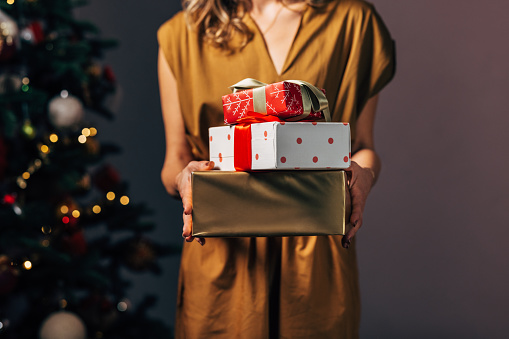 An unrecognizable Caucasian female in yellow dress holding Christmas gifts.