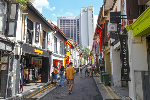 View of Haji Lane in Singapore's Kampong Glam District with tourists walking in the street and colourfully painted shop houses that have been converted into shops, cafes and bars.
