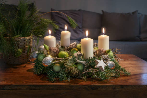 avvento, corona con quattro candele bianche accese e decorazioni natalizie su un tavolo di legno di fronte al divano, decorazioni per la casa festive, spazio per la copia, focus selezionato - advent wreath foto e immagini stock