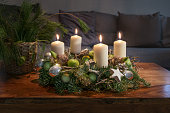 Advent, wreath with four burning white candles and Christmas decoration on a wooden table in front of the couch, festive home decor, copy space, selected focus