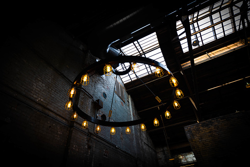 Circular chandelier in old, dark industrial building with light bulbs emitting warm light