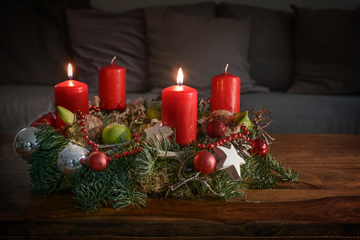 Advent wreath with two burning red candles and Christmas decoration on a wooden table in front of the couch, festive home decor for the second Sunday, copy space, selected focus, narrow depth of field