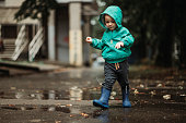 Happy boy playing outside on a rainy day wearing rubber boots and jacket