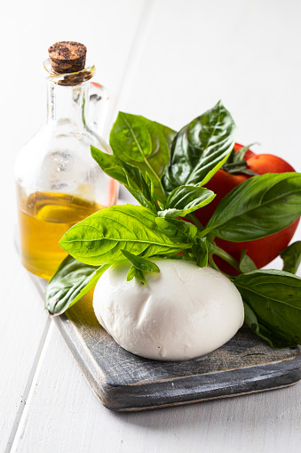 Principal ingredients of  Italian cousin,  mozzarella cheese, fresh tomatoes, basil herbs  and olive oil on wooden cut board.