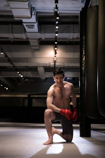 giovane pugile maschio su un ginocchio sul ring di allenamento della boxe - shirtless professional sport cheerful front view foto e immagini stock