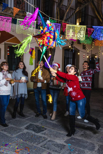 giovane donna ispanica con la famiglia messicana che rompe una piñata alla tradizionale festa di posada per natale in messico america latina - pinata mexico christmas mexican culture foto e immagini stock