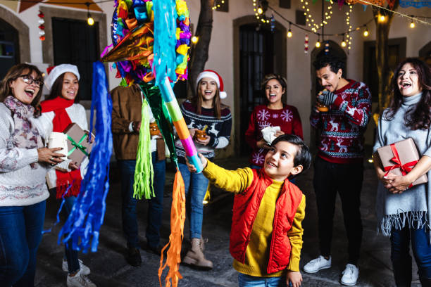bambino ispanico con la famiglia messicana che rompe una pinata alla tradizionale festa di posada per natale in messico america latina - pinata mexico christmas mexican culture foto e immagini stock