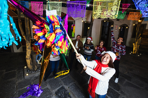 Hispanic young girl with Mexican family breaking a piñata at traditional posada party for Christmas in Mexico Latin America