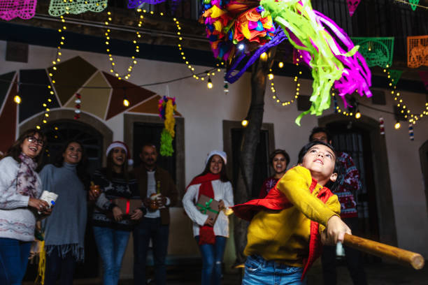 bambino ispanico con la famiglia messicana che rompe una pinata alla tradizionale festa di posada per natale in messico america latina - pinata mexico christmas mexican culture foto e immagini stock