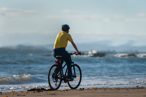 A cyclist in yellow T-shirt riding on the beach.