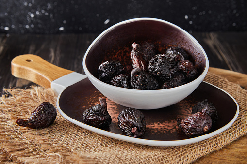 Dried mission figs in glass bowl on burlap and wooden background.