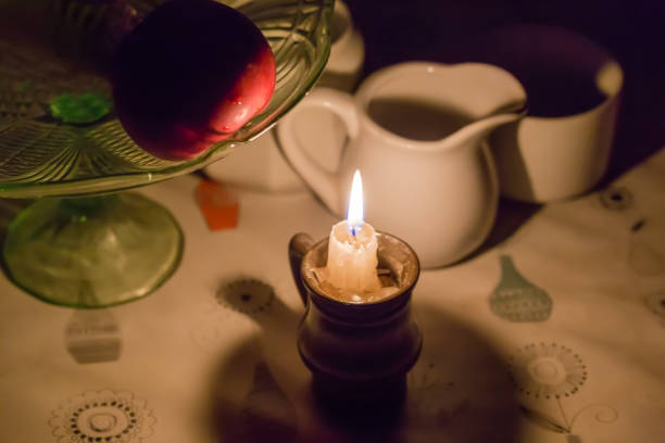Burning candle in the small candlestick on the dining table covered with oilcloth among the different crockery during a blackout