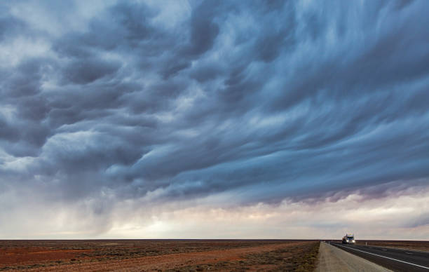 Empty road tanker heading towards camera on remote desert highway at dusk as a threatening thunderstorm develops above. Headlights on, truck is small in comparison to the storm. Concepts, ideas, metaphor