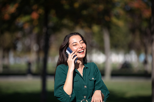 Young woman is talking someone on her mobile phone in public park.
She is very happy and smiling.