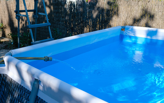 Filling a framed rectangular pool with water in a small yard on a hot day.