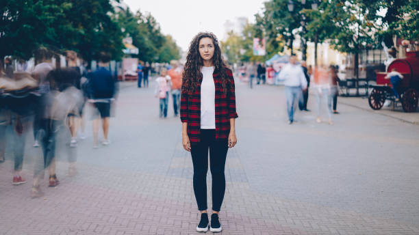 portrait of beautiful girl with long curly hair standing in street looking at camera when many men and women are walking around in hurry on summer day. - sea of tranquility imagens e fotografias de stock