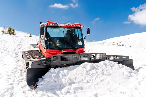 Red modern snowcat ratrack with snowplow,snow grooming machine,remover truck preparing ski slope,piste,hill at alpine skiing winter resort. Heavy machinery,tractor mountain equipment track vehicle.