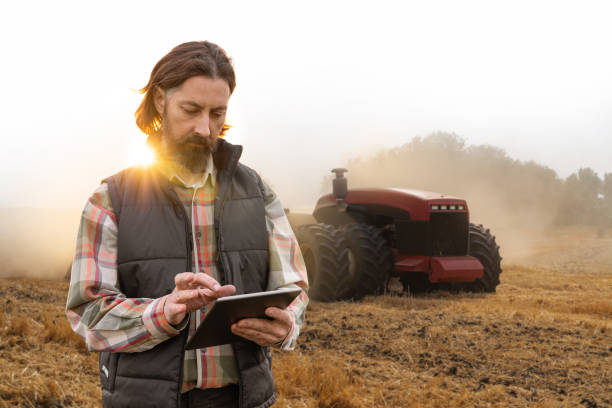 un agricultor con tableta digital controla un tractor autónomo - farmer rural scene laptop computer fotografías e imágenes de stock