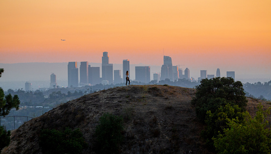 Woman standing on hill with Downtown Los Angeles cityscape in the background.