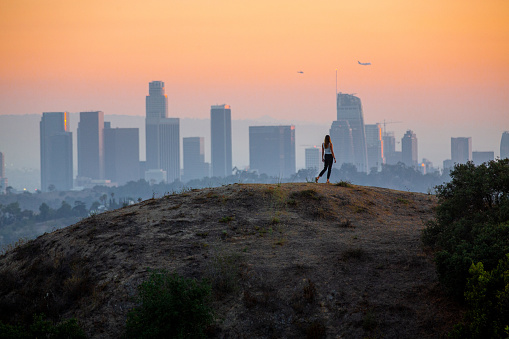 Woman standing on hill with Downtown Los Angeles cityscape in the background.