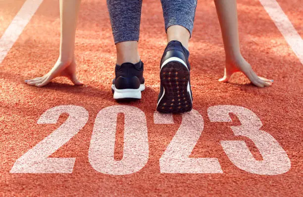 Happy new year 2023.Rear view of a woman preparing to start on an athletics track engraved with the year 2023. Start of the new year 2023, goals and plans for the next year.Opportunity, challenge,